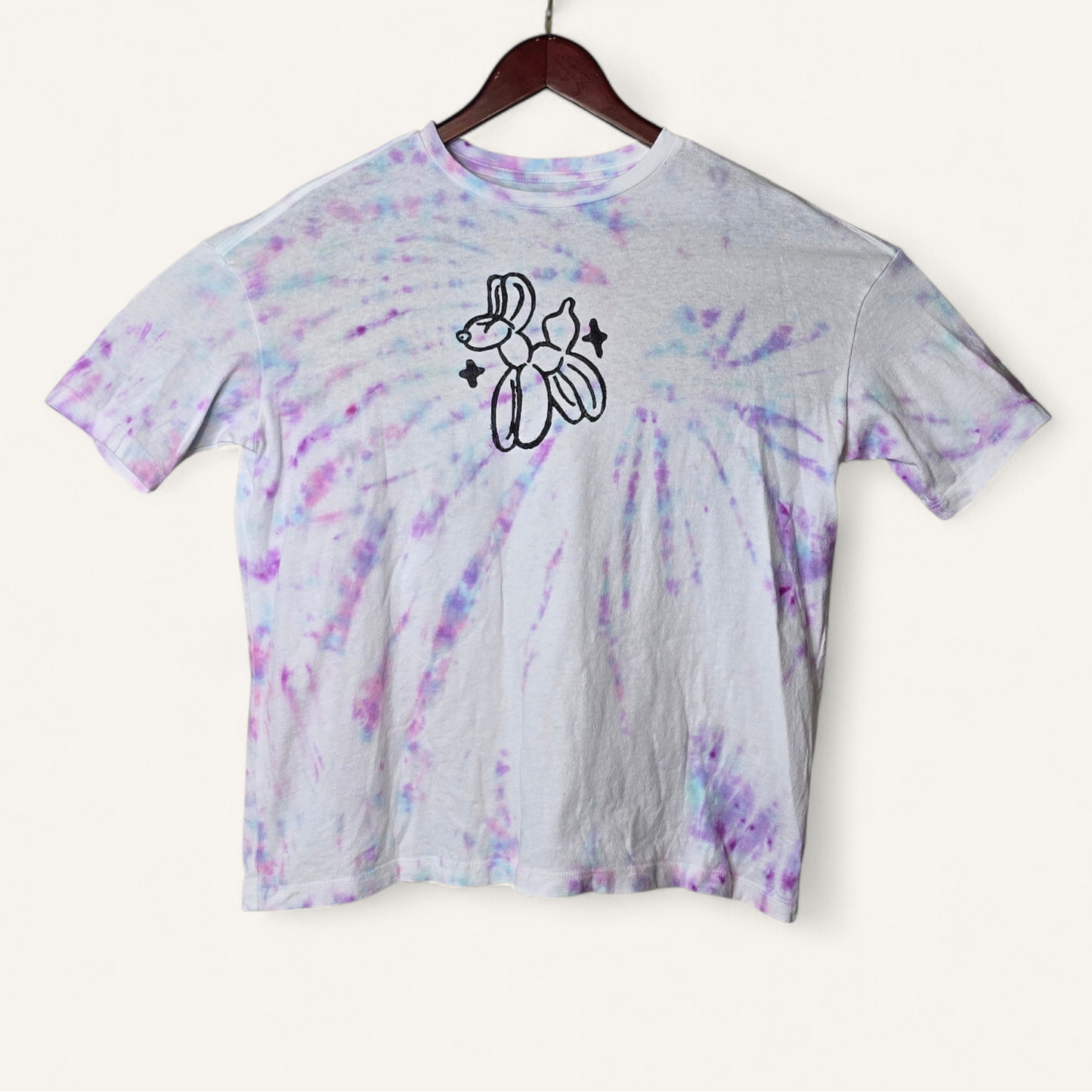 Tie-dye t-shirt with a black graphic on a hanger against a white background