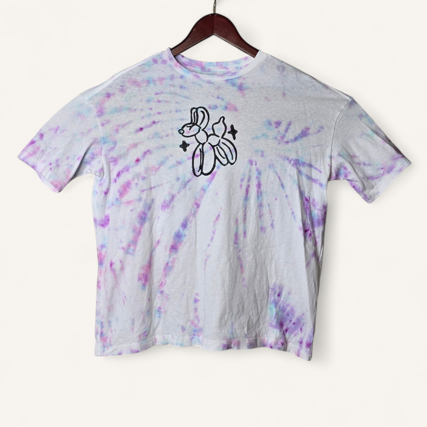 Tie-dye t-shirt with a black graphic on a hanger against a white background