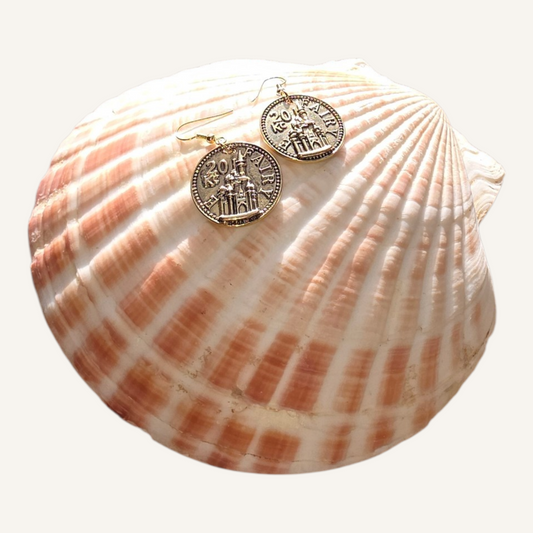Gold coin earrings on a seashell with a white background