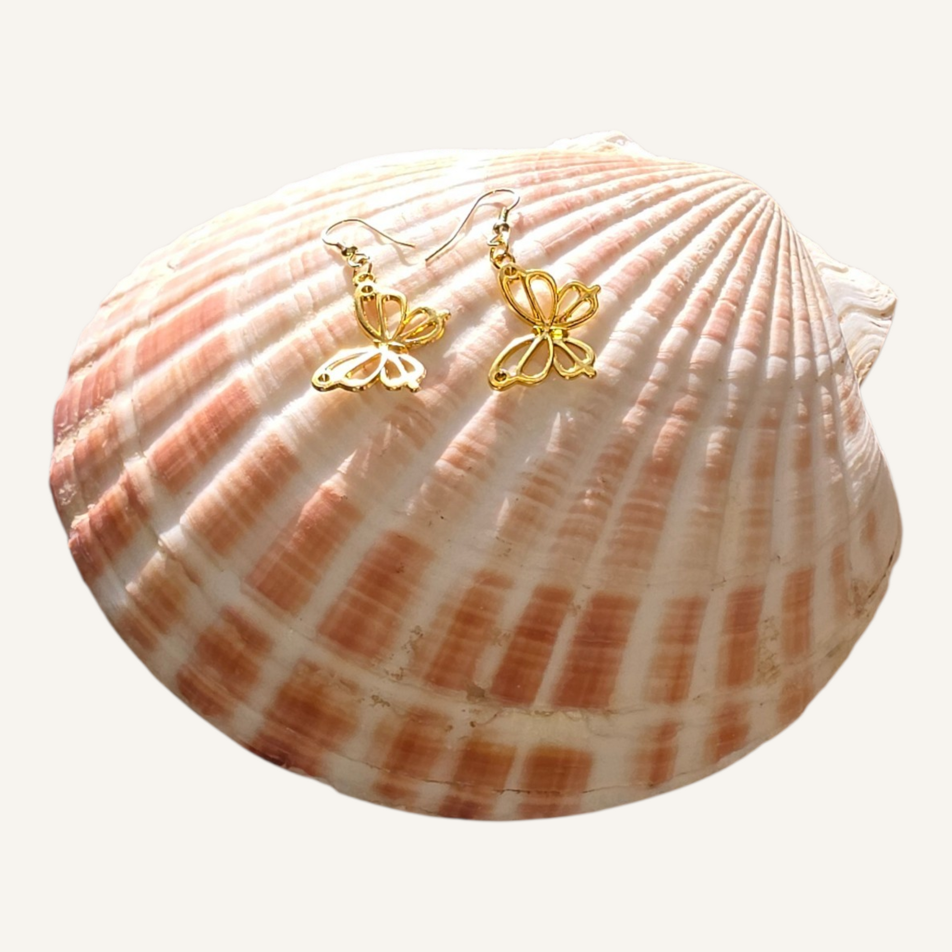 Gold butterfly earrings hanging on a gold stand against a white background