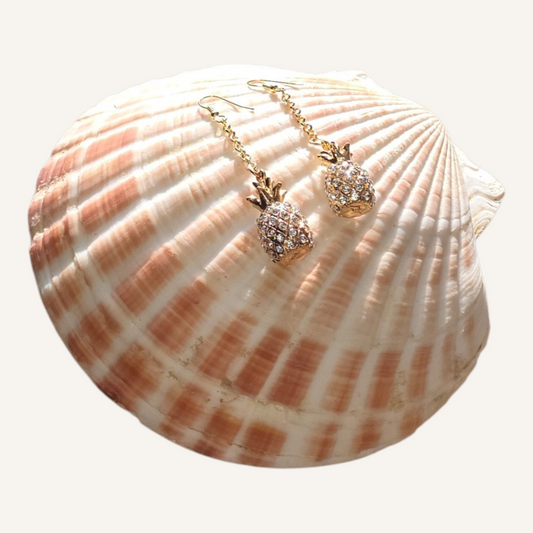 Pineapple-shaped earrings on a seashell with a white background